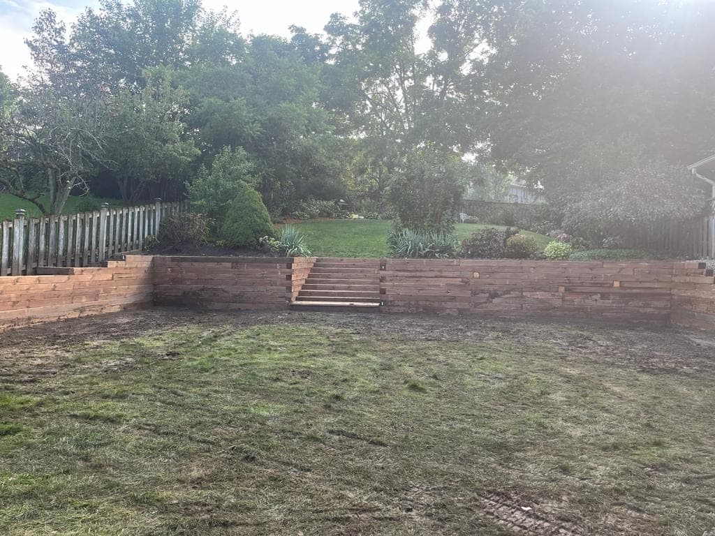 Long wood timber retaining wall with central access steps in a terraced backyard